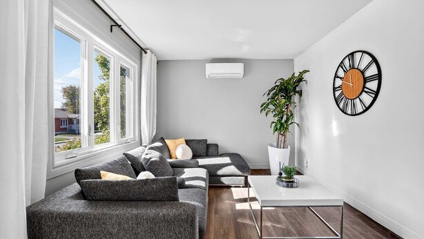 A modern living room with a sectional sofa, a coffee table, a wall clock, and a potted plant.