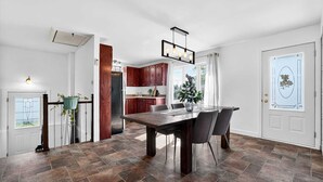 A modern kitchen with dark wooden cabinets, a large dining table, and a hanging light fixture.
