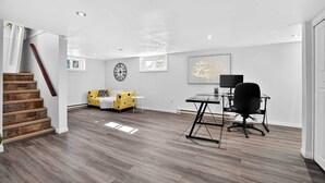 A spacious room with a wooden staircase, a yellow sofa, a desk with a chair, and a framed picture on the wall.