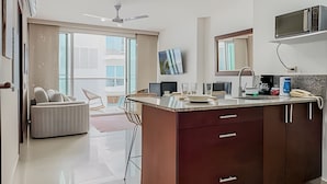 A modern kitchen with a central island, a dining area with a sofa and chairs, and a large window providing natural light. - Premium Apartment at Morros Vitri (Cartagena)