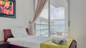 A hotel room with a bed, a red headboard, a green blanket, a white pillow, a red nightstand, a glass door leading to a balcony, and a framed artwork on the wall. - Premium Apartment at Morros Vitri (Cartagena)
