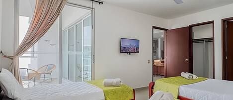 A hotel room with two beds, a TV, a ceiling fan, and a large window with curtains.