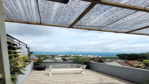 A rooftop terrace with a patterned floor, a pergola with a roof, and a view of the sea and buildings in the distance. - Cozzy Penny House Private Pool (BATU)