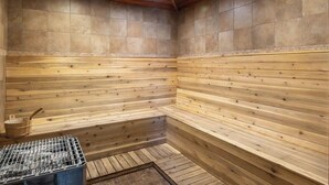 Een sauna met houten wanden en banken, een metalen rooster en een houten emmer.