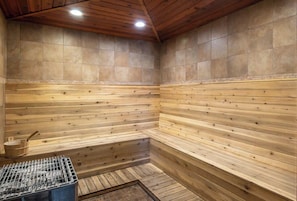 Eine Sauna mit Holzwänden und -bänken, einem Metallrost und einem Holzfass.