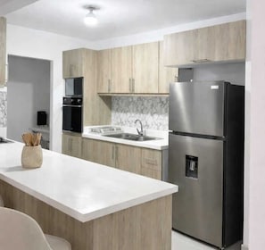 Eine moderne Küche mit Holzschränken, einem Edelstahlkühlschrank und einer Marmor-Spritzschutzwand.