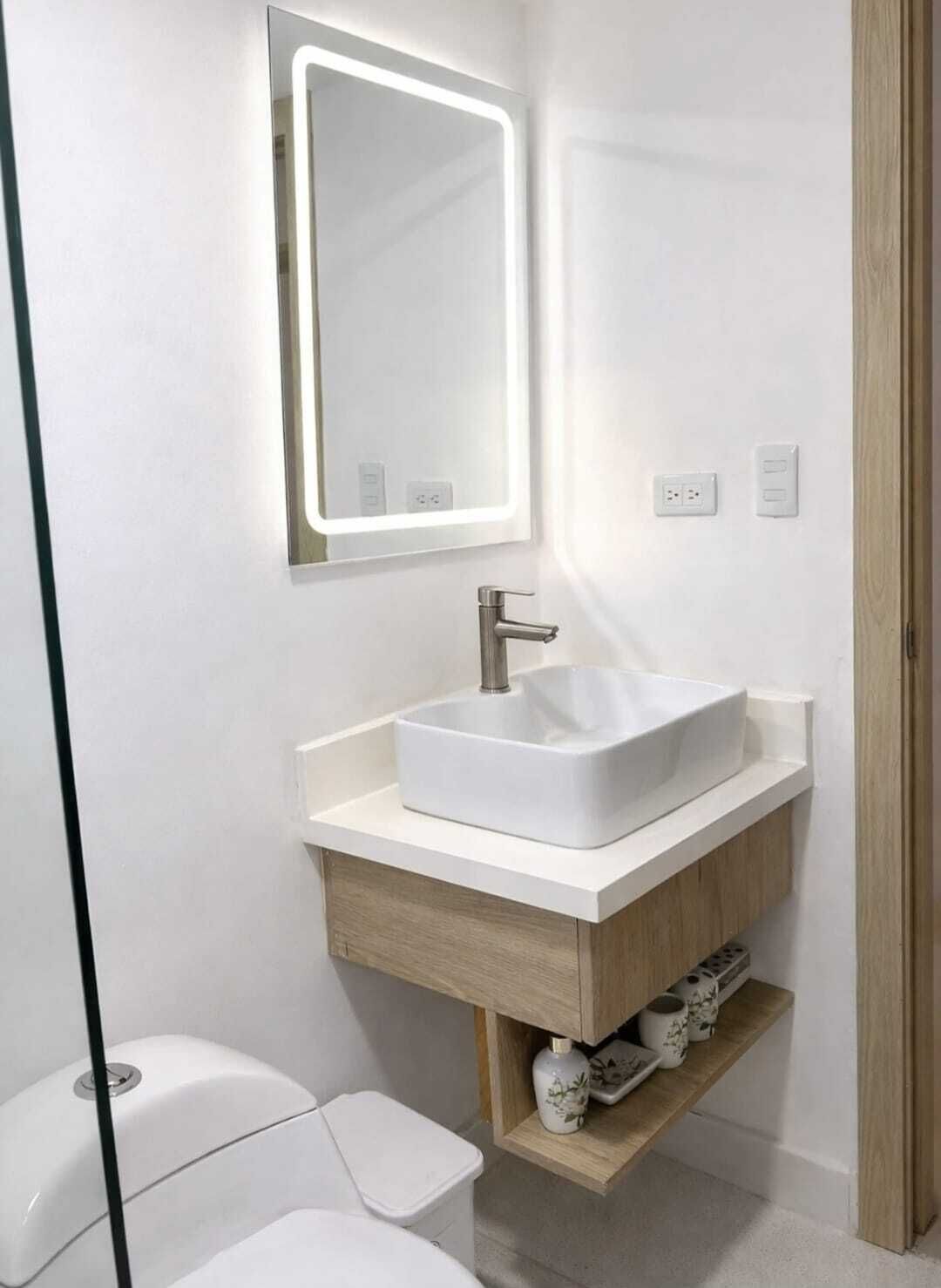 A modern bathroom with a white sink, a mirror with integrated lighting, a wooden vanity, and a toilet.