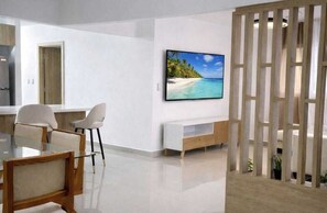 Ein modernes Wohnzimmer mit Flachbildfernseher, Glastisch und weißem Sofa.