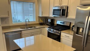 A modern kitchen with a central island, stainless steel appliances, and a window with blinds.