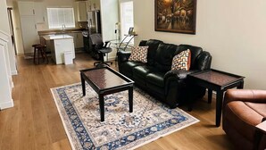 A living room with a black leather sofa, a coffee table, a patterned rug, and a painting on the wall.