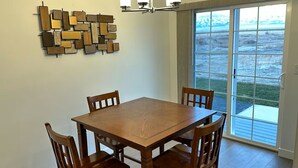 A dining area with a wooden table and chairs, a wall-mounted light fixture, and a large window with a view.