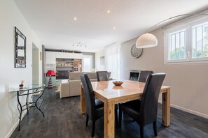 Un coin repas avec une table et des chaises en bois, une table basse en verre et, au fond, une cuisine moderne.