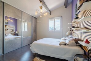 Une chambre à coucher avec un grand lit, un miroir, un lustre, une fenêtre et une étagère ornée d’objets décoratifs.