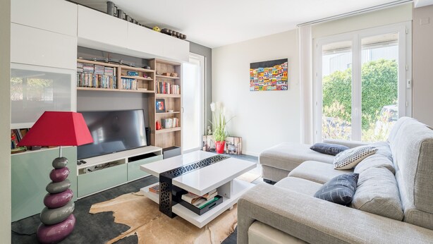 Ein modernes Wohnzimmer mit Sofa, Couchtisch, Fernseher und Bücherregalen.