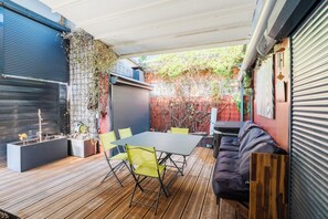 Une terrasse couverte avec une table et des chaises, un canapé et des jardinières avec des plantes.