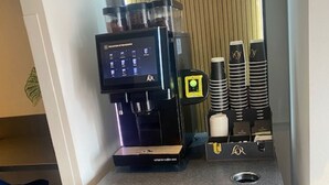 Una cafetera con pantalla digital, tazas apiladas y un cubo de basura.
