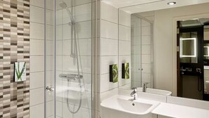 Un baño moderno con ducha de vidrio, dos lavamanos y un espejo grande.