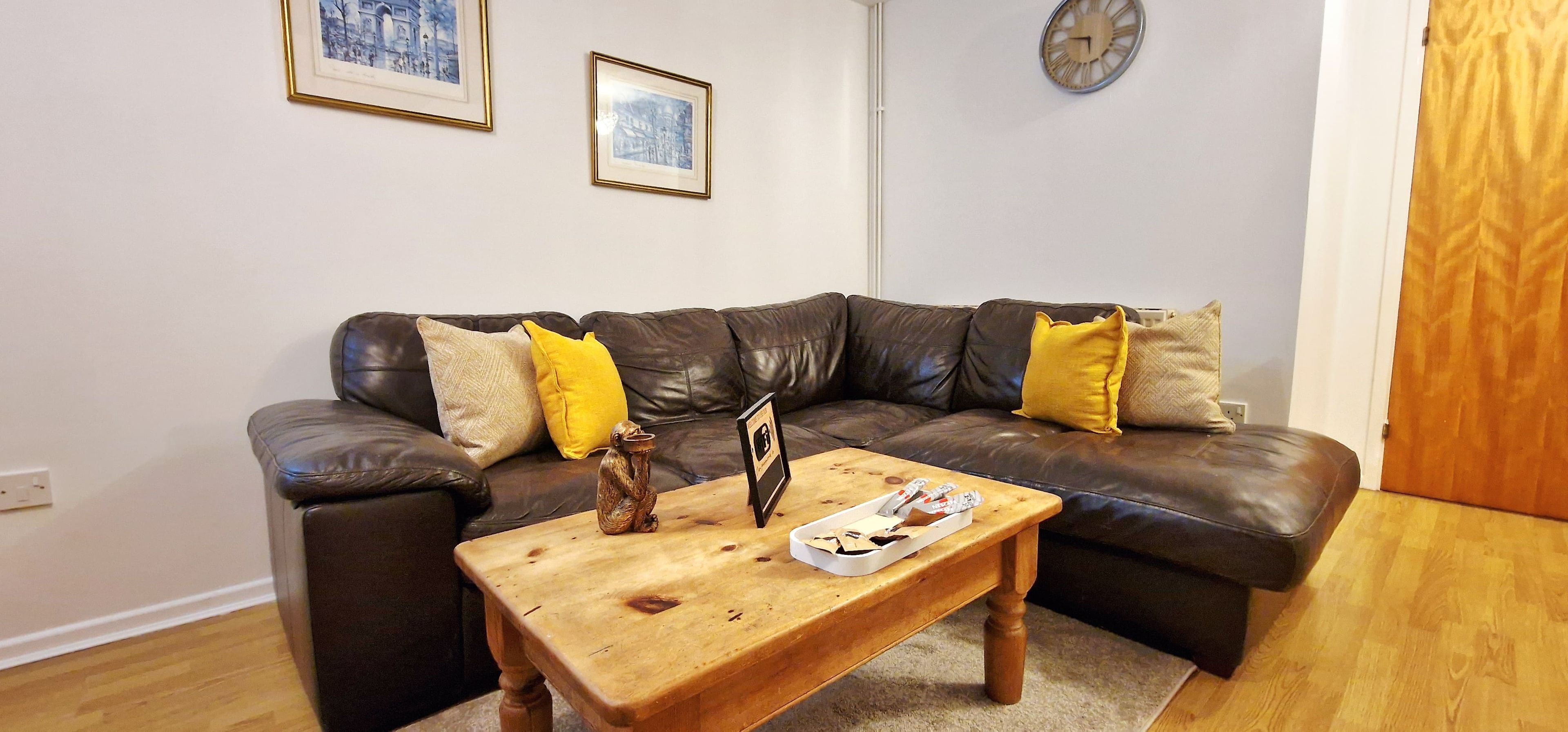 A living room with a leather sofa, a wooden coffee table, and two framed pictures on the wall.