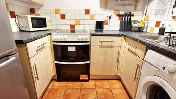 A compact kitchen with a microwave, oven, washing machine, and a tiled backsplash.
