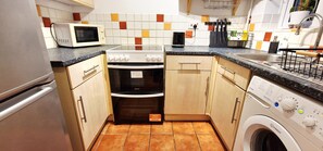 Eine kompakte Küche mit Mikrowelle, Backofen, Waschmaschine und gefliestem Spritzschutz.