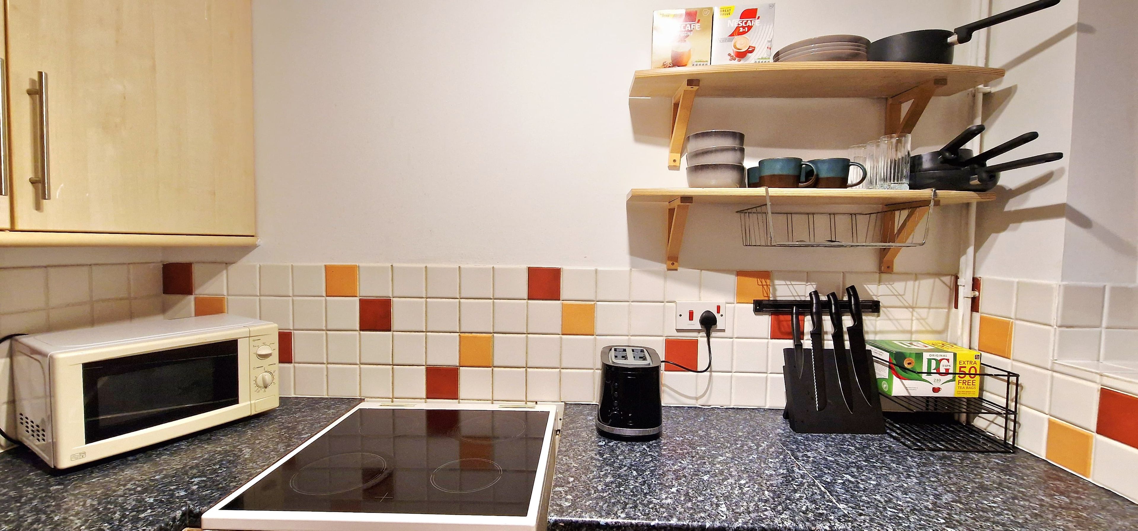 A kitchen with a microwave, a toaster, and a kettle on the counter.