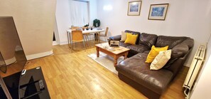 A living room with a brown leather sofa, wooden coffee table, and a dining area with a white table and chairs.