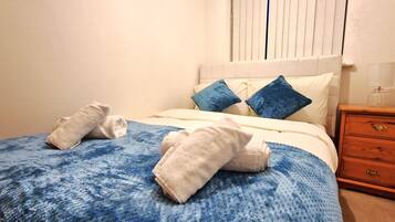Een net opgemaakt bed met een blauw-witte bedspreide, twee kussens en twee opgerolde handdoeken op het bed.