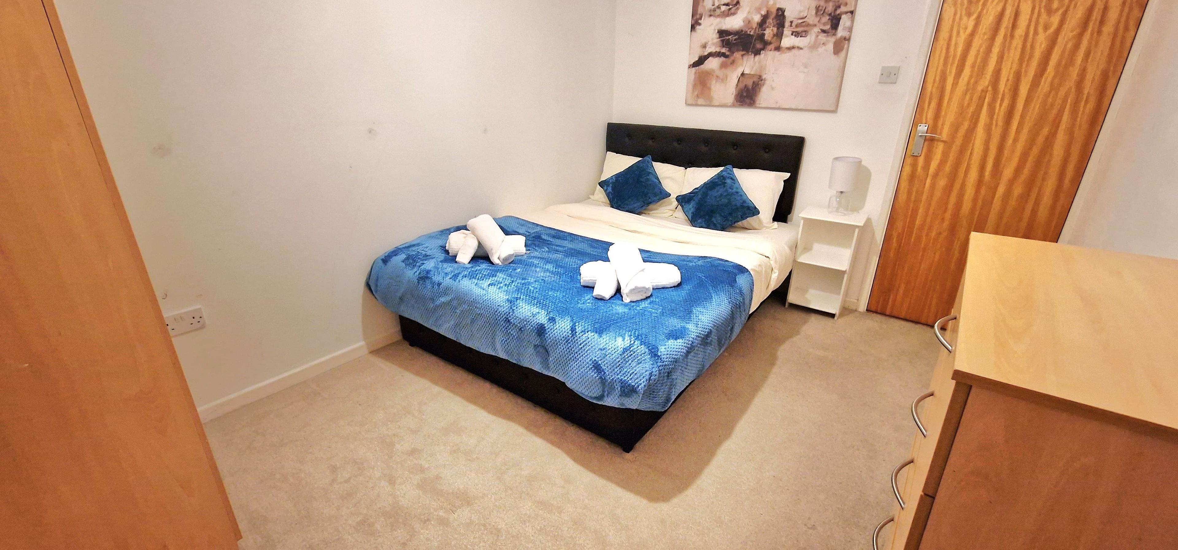 A neatly made bed with a blue and white bedspread, a black headboard, and two white towels on the bed.