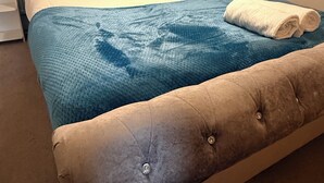 Ein Bett mit einer gepolsterten Kopfteile, zwei Kissen, einer blauen Decke und einem aufgerollten weißen Handtuch.