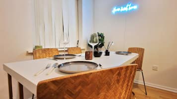 A dining area with a white table, wooden chairs, and a neon sign on the wall.