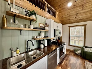 Una cocina con estantes de madera, un lavaplatos, un microondas y una ventana con vistas.