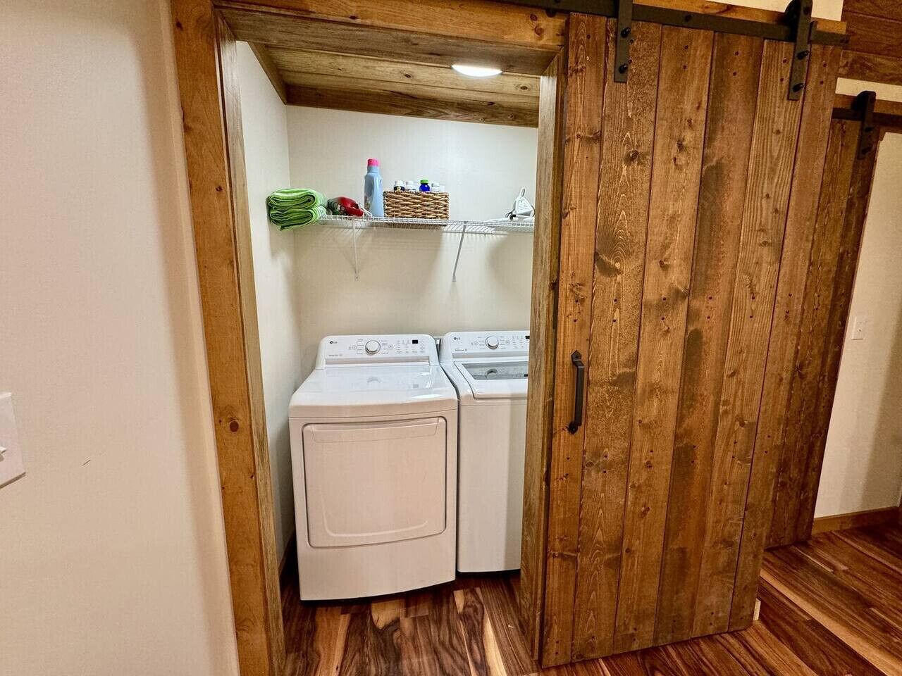 Une buanderie équipée de deux machines à laver, d’une porte en bois et d’une étagère contenant des produits de lessive.