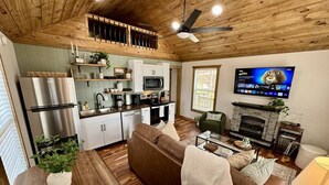 A modern kitchen with stainless steel appliances, a dining area with a wooden table and chairs, a living room with a sofa and fireplace, and a TV mounted on the wall. - Alone At Last (Campton)