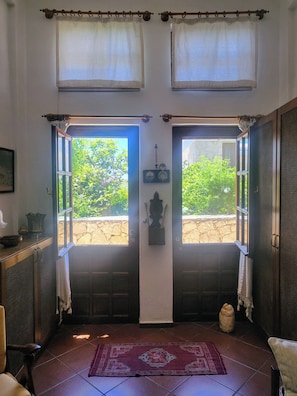 Ein Zimmer mit Doppeltüren, Fliesenboden, Teppich und Blick auf Grünfläche.