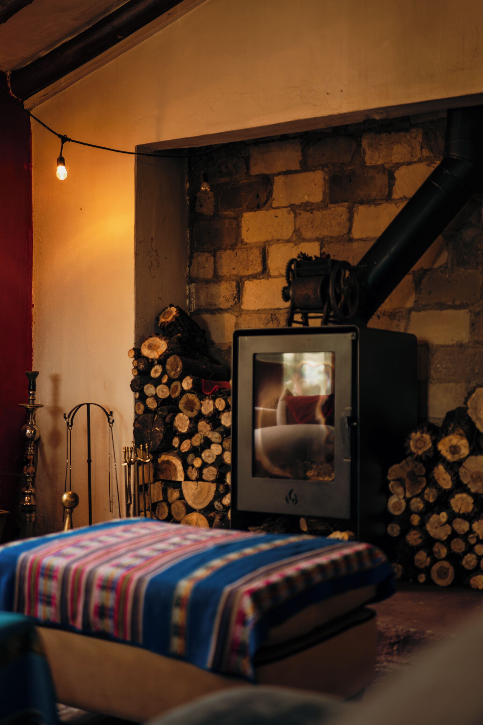 Una habitación acogedora con una cama, un estufa de leña y una pared llena de leña apilada.
