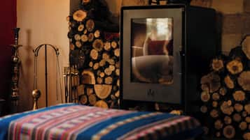 Una habitación acogedora con una cama, un estufa de leña y una pared llena de leña apilada.