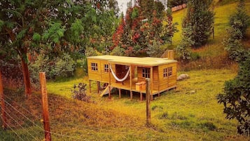 Une cabane en bois dotée d’un porche, entourée d’arbres et d’une colline verdoyante.