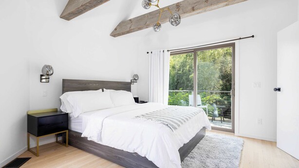 A bedroom with a bed, bedside table, and a view of greenery through a sliding door. - Dumar Villa by Rove - 6BR Family Home With Pool & Outdoor Spaces (Sag Harbor)