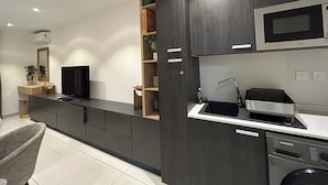 Una cocina moderna con armarios oscuros, microondas integrado, lavavajillas y una estantería de madera con libros y objetos decorativos.