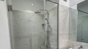 Un baño moderno con cabina de ducha de vidrio, un lavamanos blanco y un espejo grande.