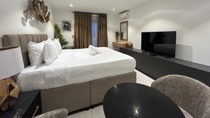 Habitación de hotel con cama, mesita de noche, televisor y una pequeña zona de comedor.