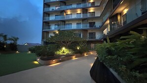 Un hotel de varios pisos con balcones, un jardín ajardinado y un camino.