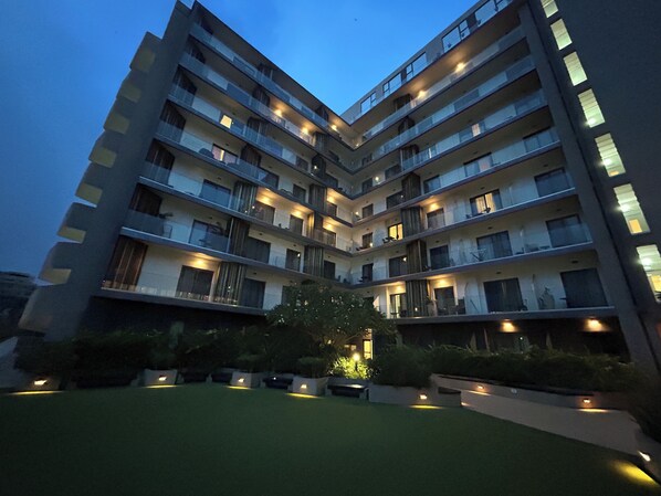 Un edificio de varios pisos con balcones, un patio central con plantas e iluminación exterior.