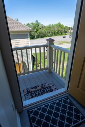 A balcony with a white railing, a doormat with 'HOME' written on it, and a clear view of a street with cars and greenery. - Near Downtown, Hospitals (Roanoke)