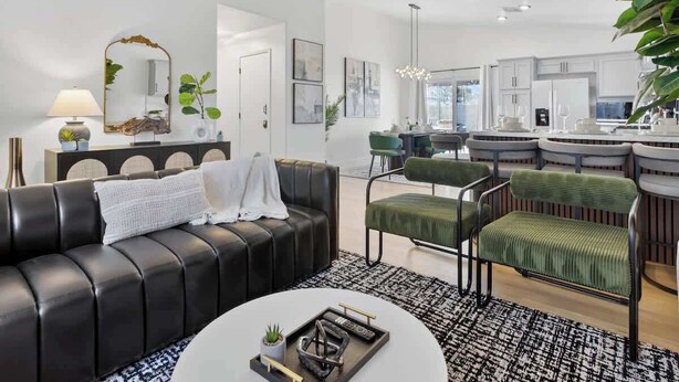 Un soggiorno moderno con un divano in pelle nera, poltrone rivestite in verde, un tavolino rotondo e una cucina sullo sfondo.