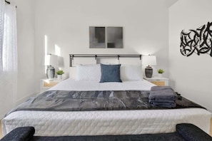 A neatly made bed with a quilted mattress, two bedside lamps, and a wall art piece. - Luxury Arcade Retreat for 16 in North LV! (North Las Vegas)