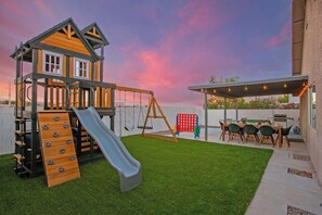 A children's play area with a slide, swings, and a climbing structure. - Luxury Arcade Retreat for 16 in North LV! (North Las Vegas)