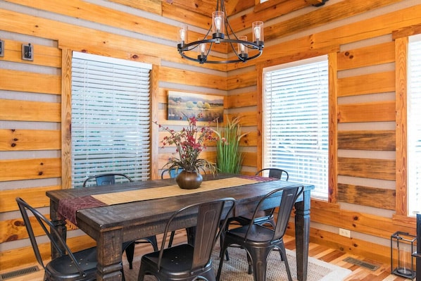 A wooden-paneled room with a dining table, chairs, a chandelier, and a potted plant.