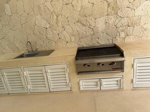 A kitchen with a stone backsplash, a stainless steel sink, and a built-in grill. - Santa Akumalito (Tulum)