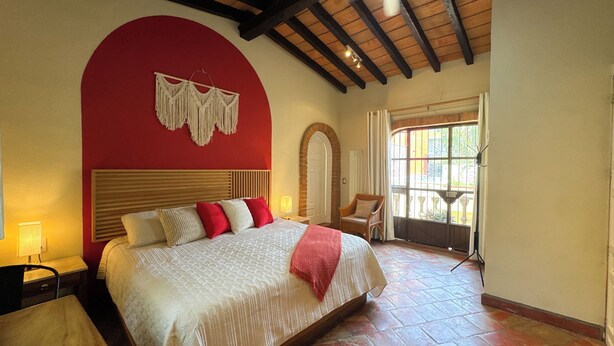Een slaapkamer met een groot bed, een houten plafond, een rode wand en een raam met uitzicht.